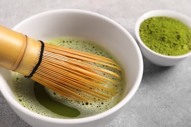 Photo of Cup of matcha tea and bamboo whisk on light gray table, closeup