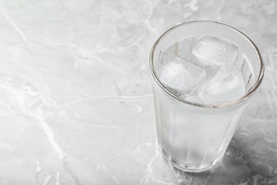 Photo of Glass of soda water with ice on grey table. Space for text