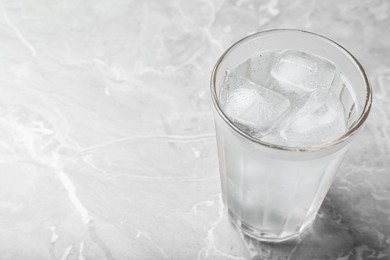 Glass of soda water with ice on grey table. Space for text