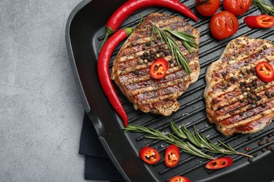 Grill pan with delicious pork steaks, spices and vegetables on grey table, top view