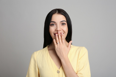 Photo of Emotional young woman wearing beautiful engagement ring on grey background