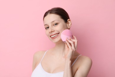 Photo of Washing face. Young woman with cleansing brush on pink background