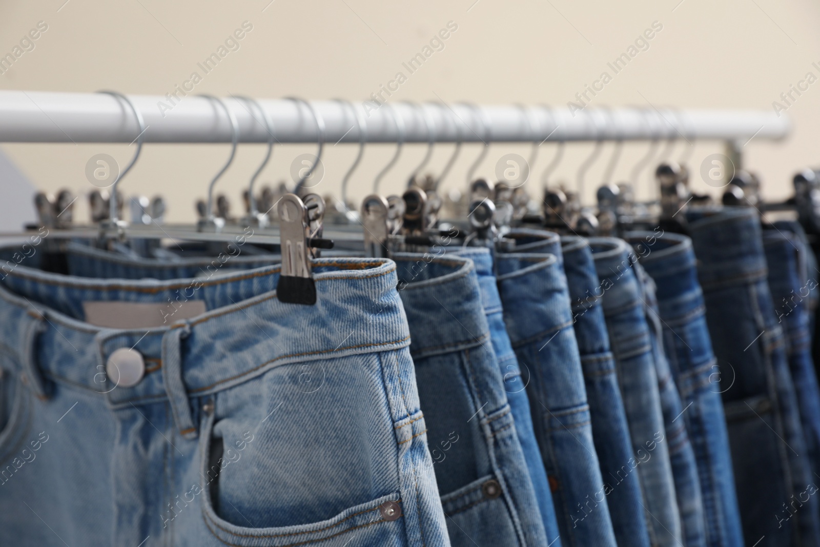 Photo of Rack with stylish jeans on beige background, closeup