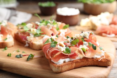 Photo of Delicious sandwiches with prosciutto, cheese and microgreens on wooden table, closeup