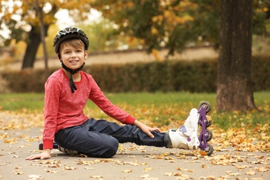 Cute boy with roller skates sitting on road in park