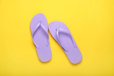 Stylish violet flip flops on yellow background, top view