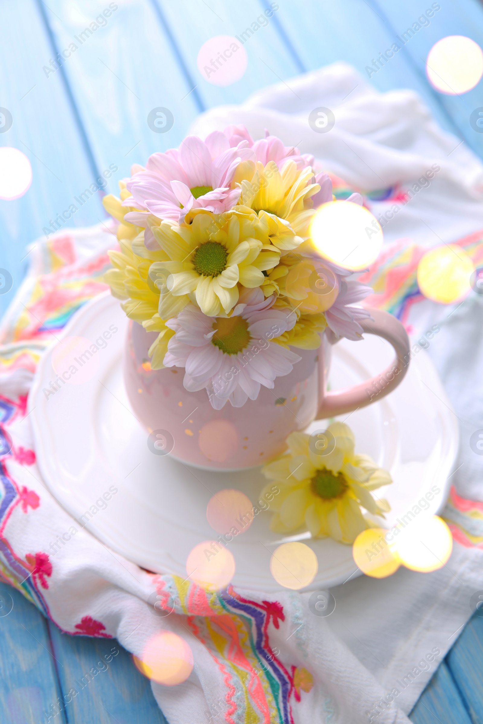 Photo of Bouquet of beautiful flowers in cup on light blue wooden table