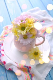 Bouquet of beautiful flowers in cup on light blue wooden table