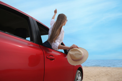 Happy woman leaning out of car window on beach. Summer vacation trip