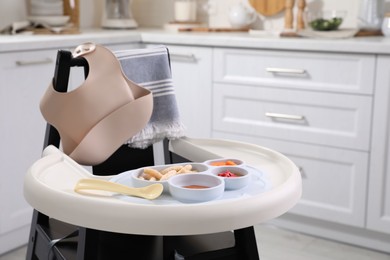 Photo of High chair with food in baby tableware on tray indoors