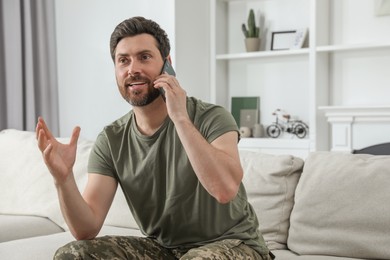 Photo of Happy soldier talking on phone in living room. Military service