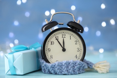 Photo of Vintage alarm clock with decor on light blue wooden table against blurred Christmas lights, closeup. New Year countdown