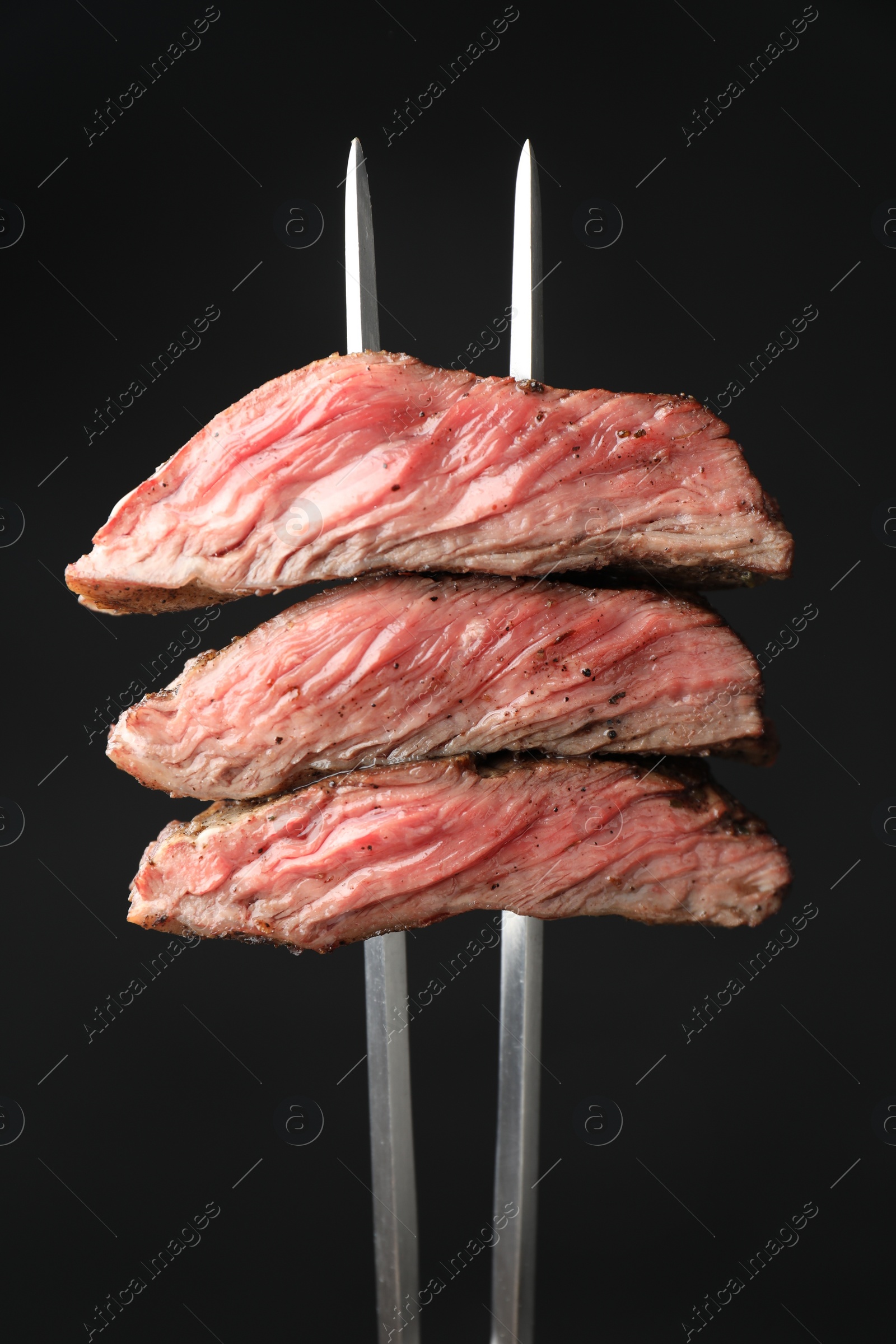 Photo of Meat fork with grilled beef pieces on black background, closeup