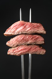 Photo of Meat fork with grilled beef pieces on black background, closeup