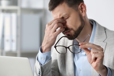 Man suffering from eyestrain in office, focus on hand with glasses