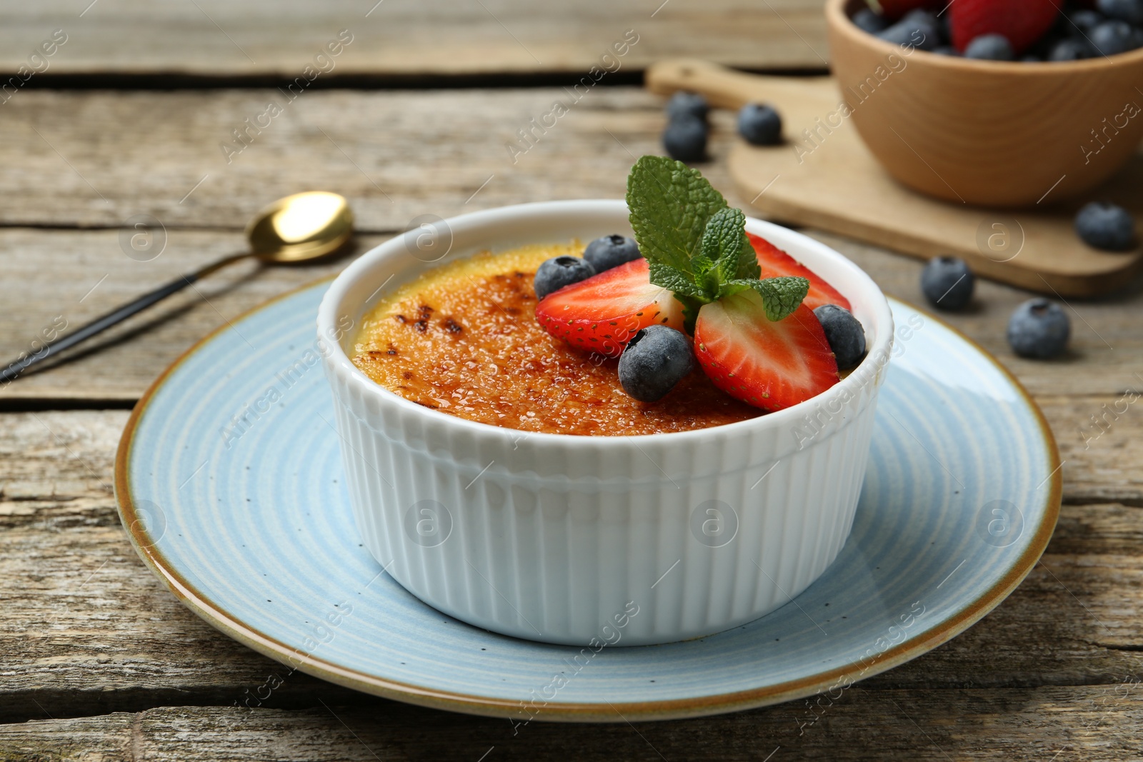 Photo of Delicious creme brulee with berries and mint in bowl on wooden table, closeup