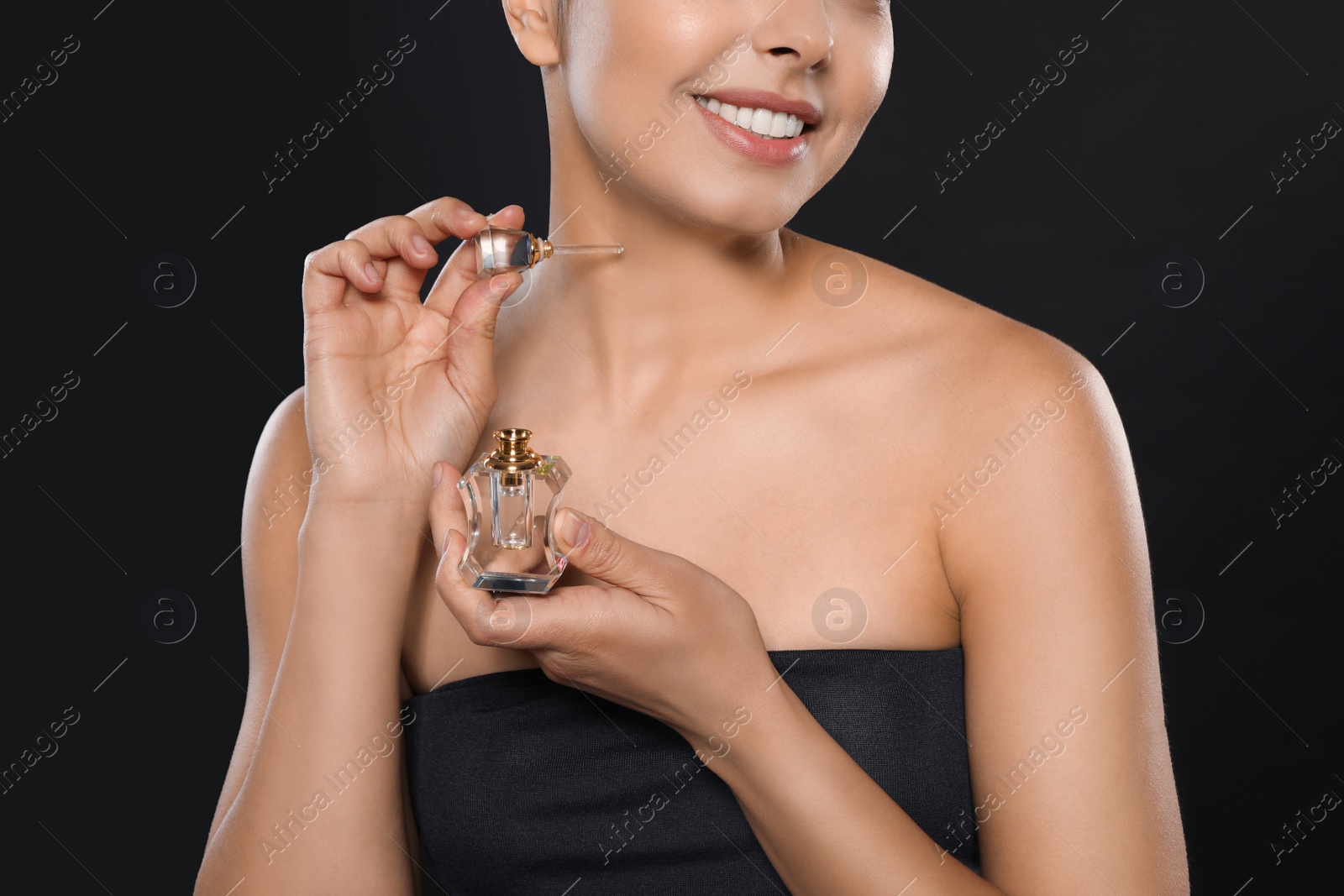 Photo of Young woman applying perfume on black background, closeup