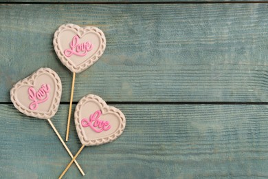 Photo of Chocolate heart shaped lollipops with word Love on light blue wooden table, flat lay. Space for text