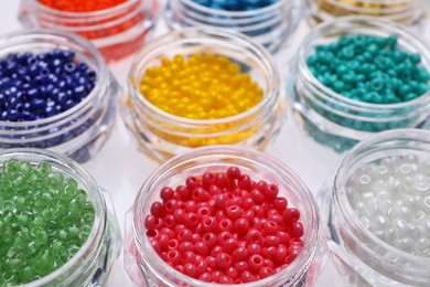 Photo of Plastic containers with different beads on white background, closeup