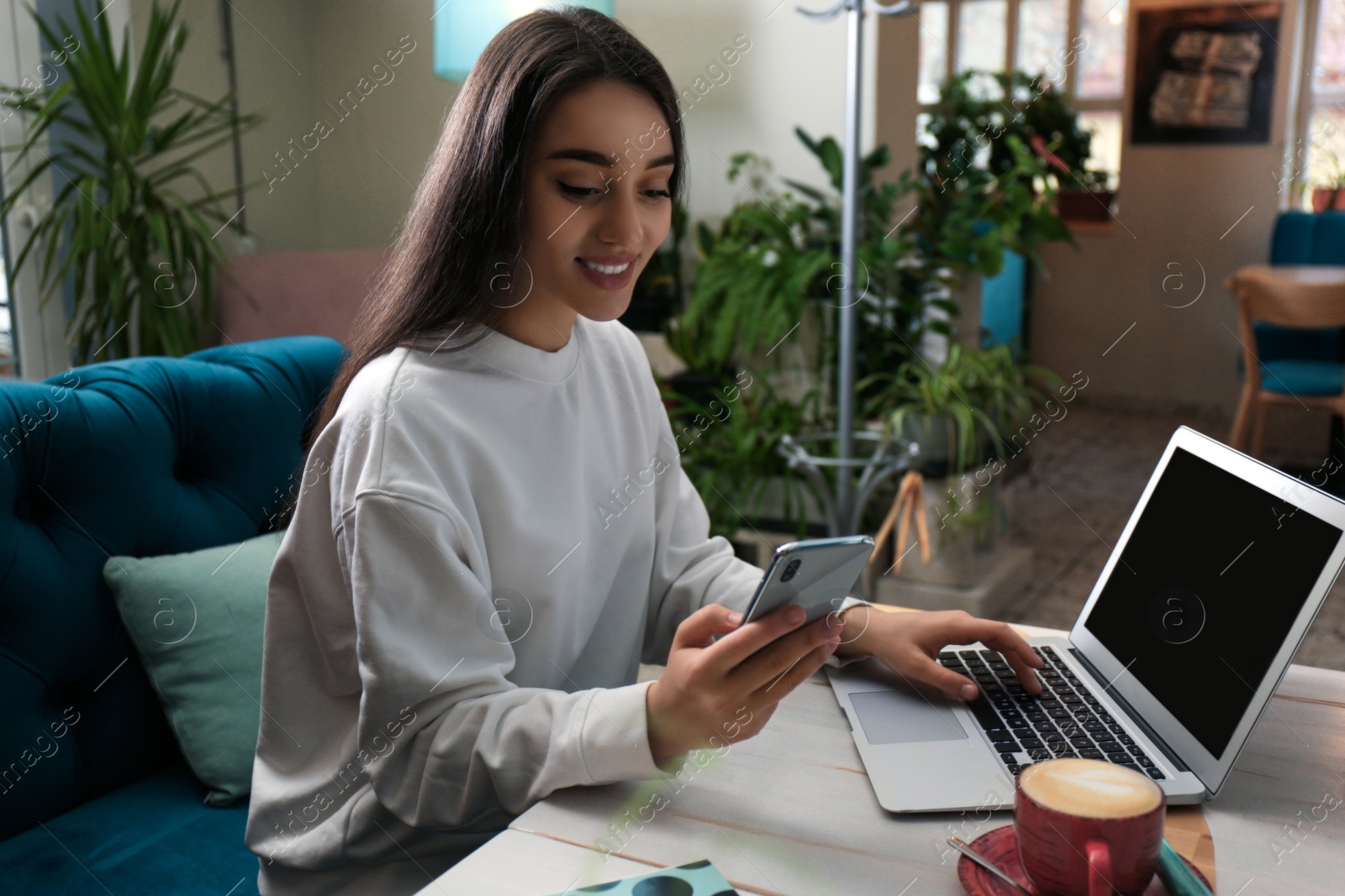 Photo of Young blogger with laptop and smartphone in cafe