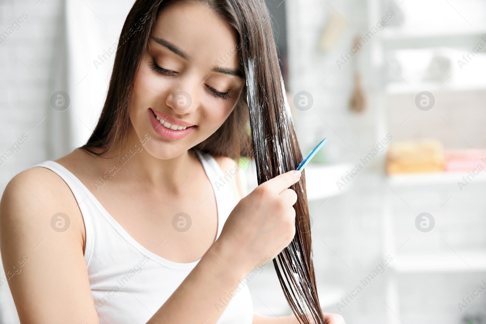 Photo of Young woman brushing hair after applying mask in bathroom