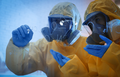 Photo of Scientists in chemical protective suits writing formula on glass board at laboratory. Virus research