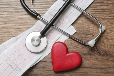 Photo of Cardiogram report, red heart and stethoscope on wooden table, flat lay