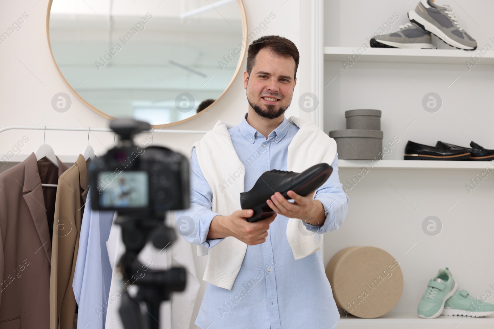Photo of Smiling fashion blogger showing shoe while recording video at home