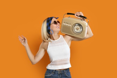 Photo of Happy hippie woman with retro radio receiver dancing on orange background