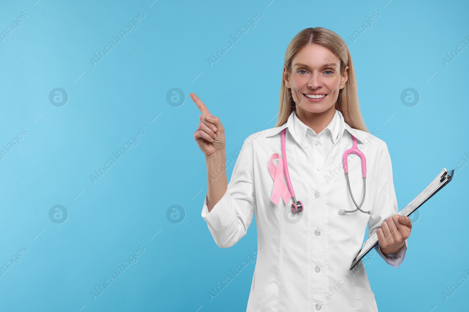 Photo of Doctor with pink ribbon, clipboard and stethoscope on light blue background, space for text. Breast cancer awareness