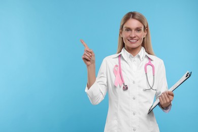 Photo of Doctor with pink ribbon, clipboard and stethoscope on light blue background, space for text. Breast cancer awareness