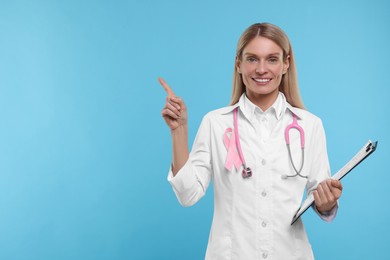 Doctor with pink ribbon, clipboard and stethoscope on light blue background, space for text. Breast cancer awareness