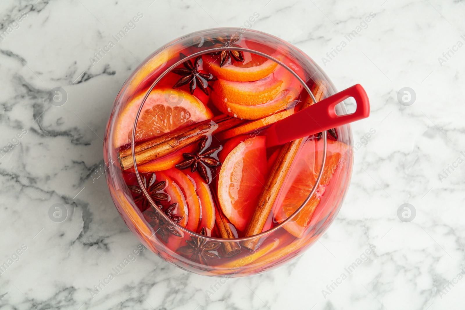 Photo of Glass and bowl of delicious aromatic punch drink on white marble table, top view