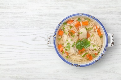 Photo of Homemade chicken soup served on wooden background, top view with space for text