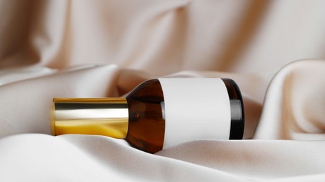 Luxury bottle of perfume on beige silk, closeup