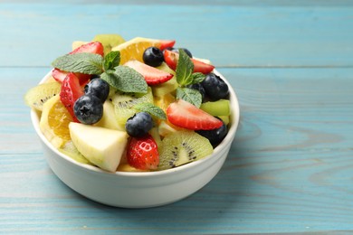 Photo of Tasty fruit salad in bowl on light blue wooden table, closeup. Space for text