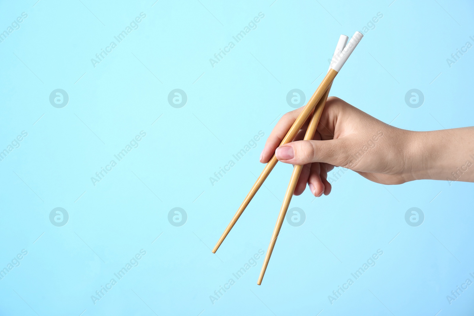 Photo of Woman holding pair of wooden chopsticks on light blue background, closeup. Space for text