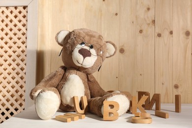 Dyslexia concept. Teddy bear with glasses and wooden letters on light table, space for text