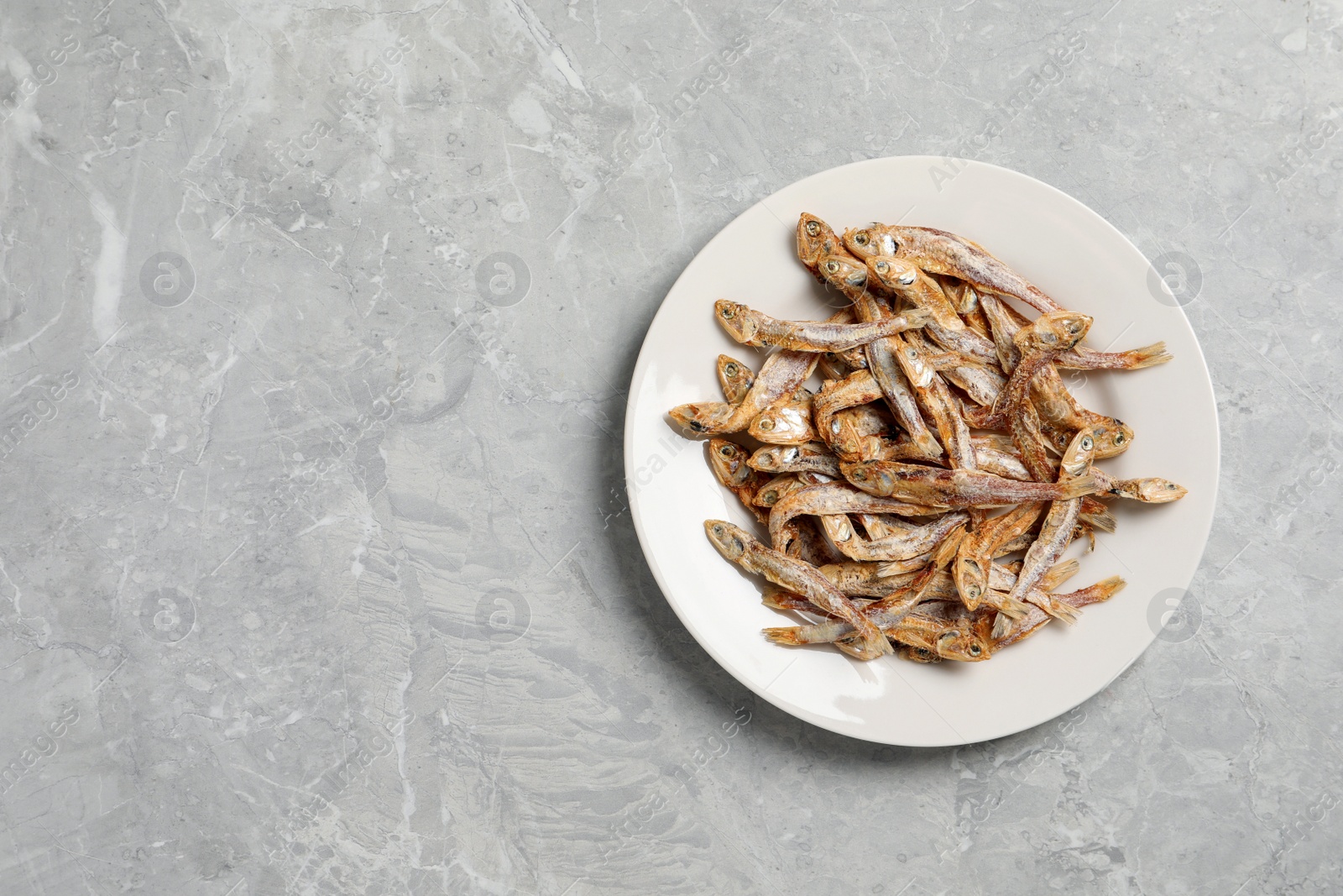 Photo of Plate of tasty dried anchovies on light grey marble table, top view. Space for text