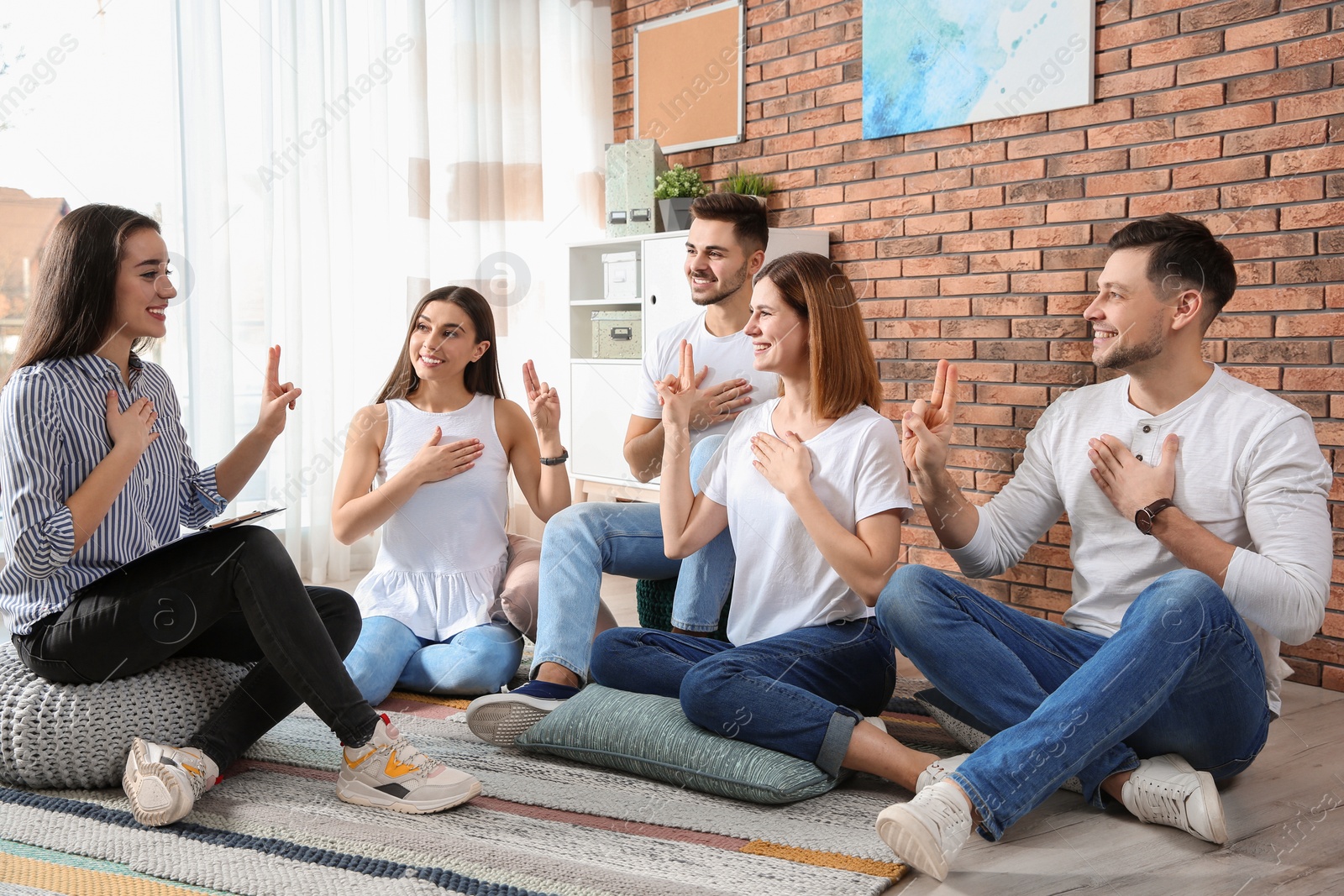 Photo of Group of young people learning sign language with teacher indoors