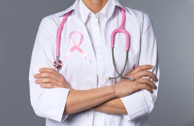Photo of Female doctor with pink ribbon and stethoscope on grey background, closeup. Breast cancer concept