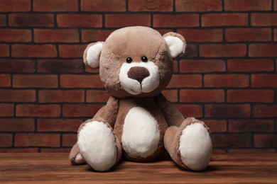 Cute teddy bear on wooden table near brick wall