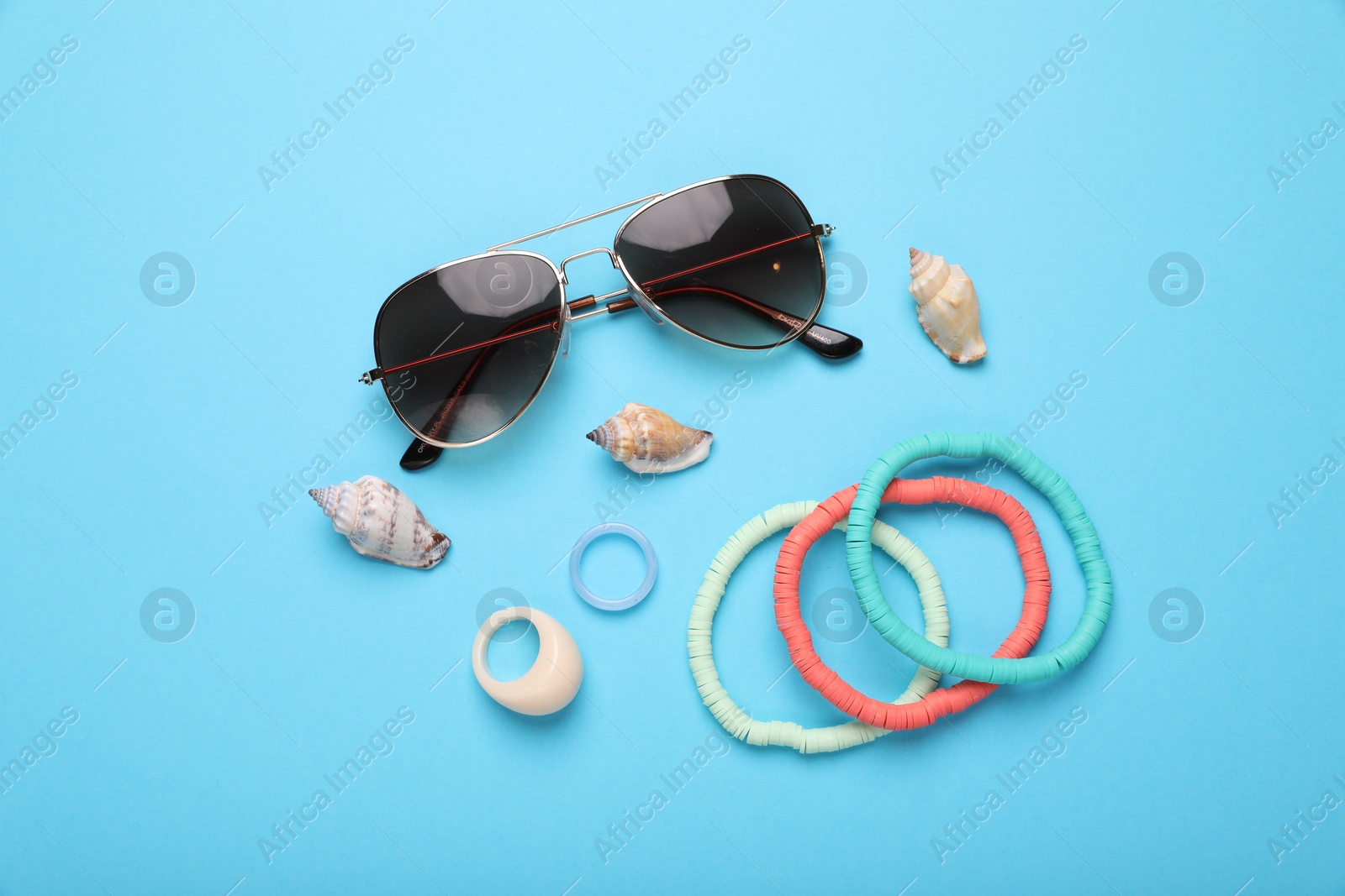 Photo of Stylish sunglasses, bracelets, seashells and rings on light blue background, flat lay