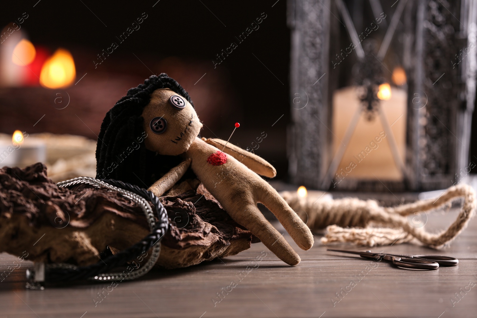Photo of Female voodoo doll with pin in heart and ceremonial items on wooden table