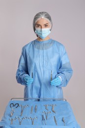 Photo of Doctor holding surgical instruments near table on light background
