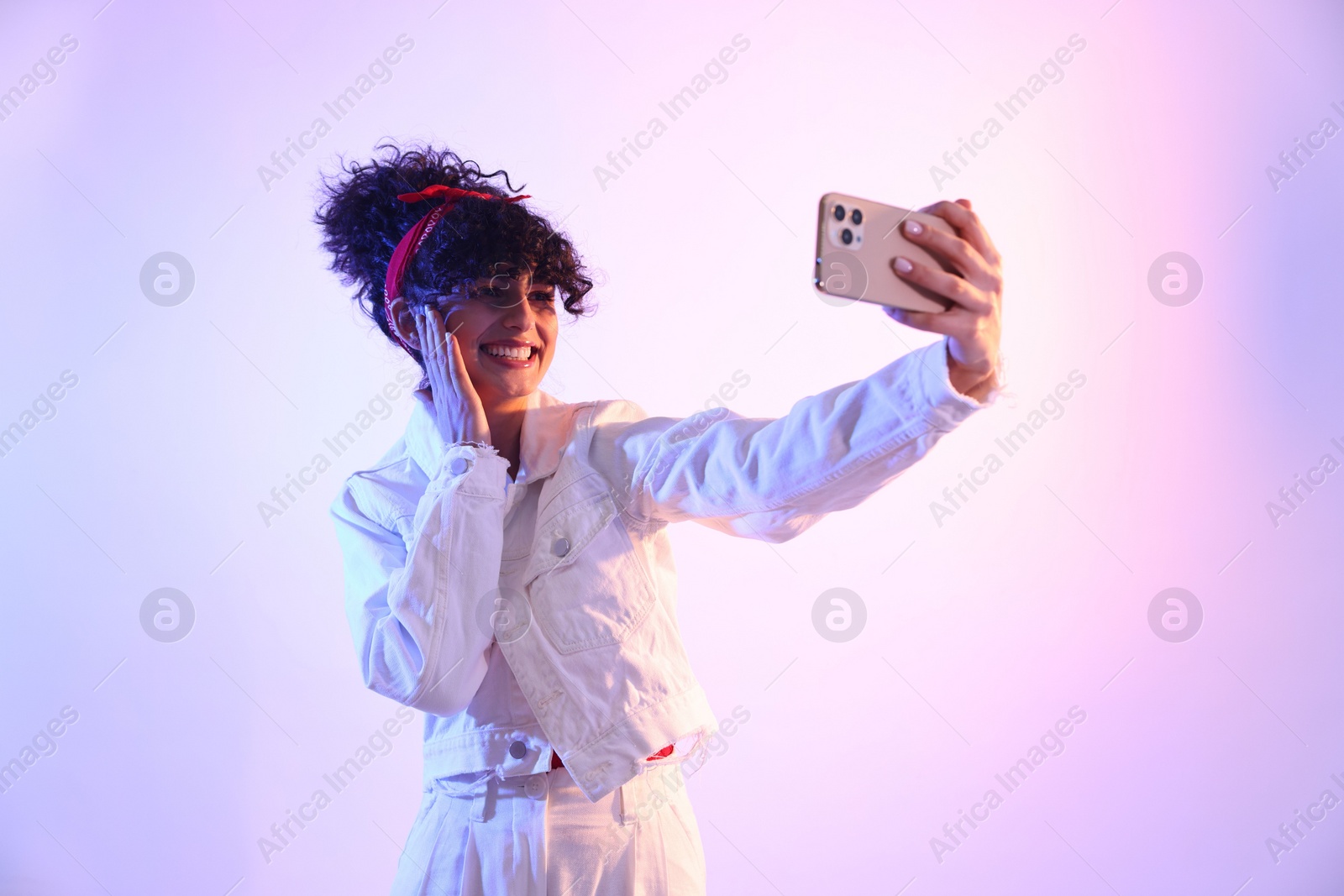 Photo of Beautiful young woman taking selfie on color background in neon lights