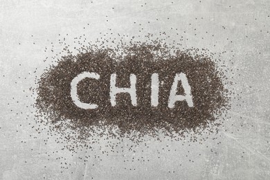 Word CHIA written in pile of seeds on grey table, top view