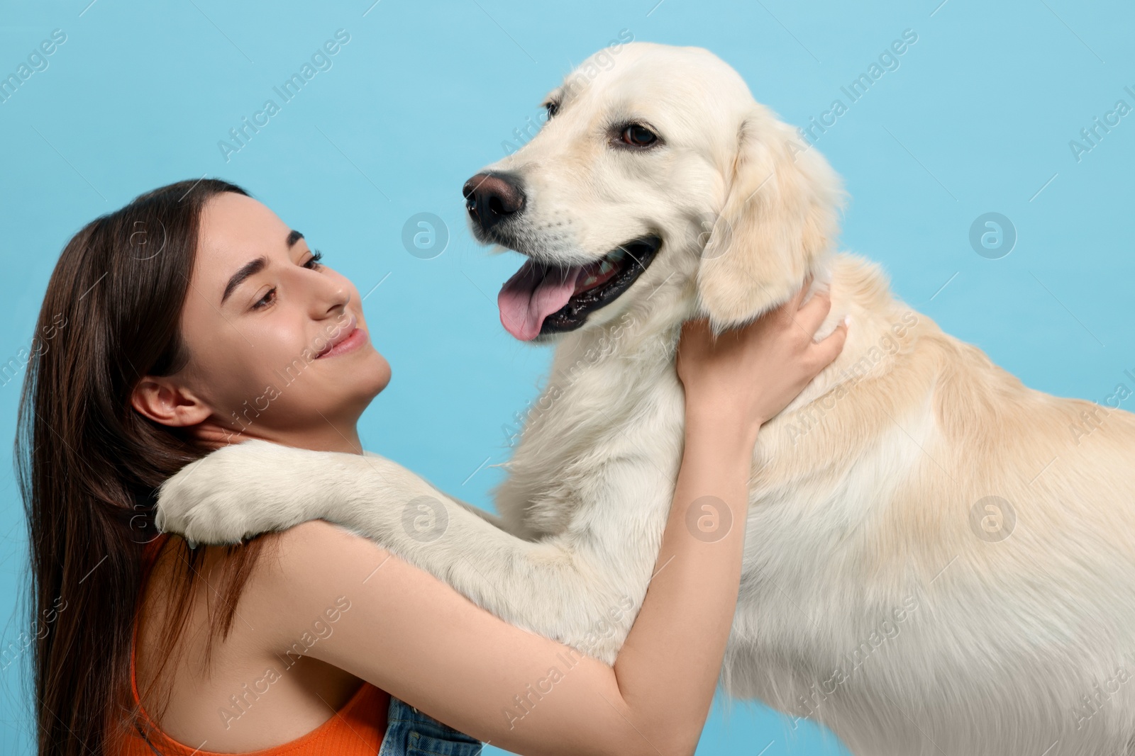 Photo of Happy woman with cute Labrador Retriever dog on light blue background. Adorable pet