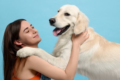 Happy woman with cute Labrador Retriever dog on light blue background. Adorable pet