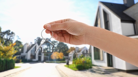 Real estate agent holding key against modern houses, closeup. Banner design
